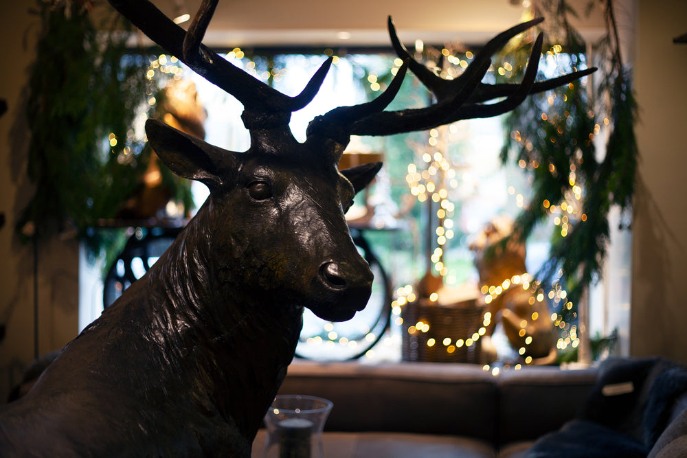 A life sized stag made from bronze with a background of christmas lights and shop window display
