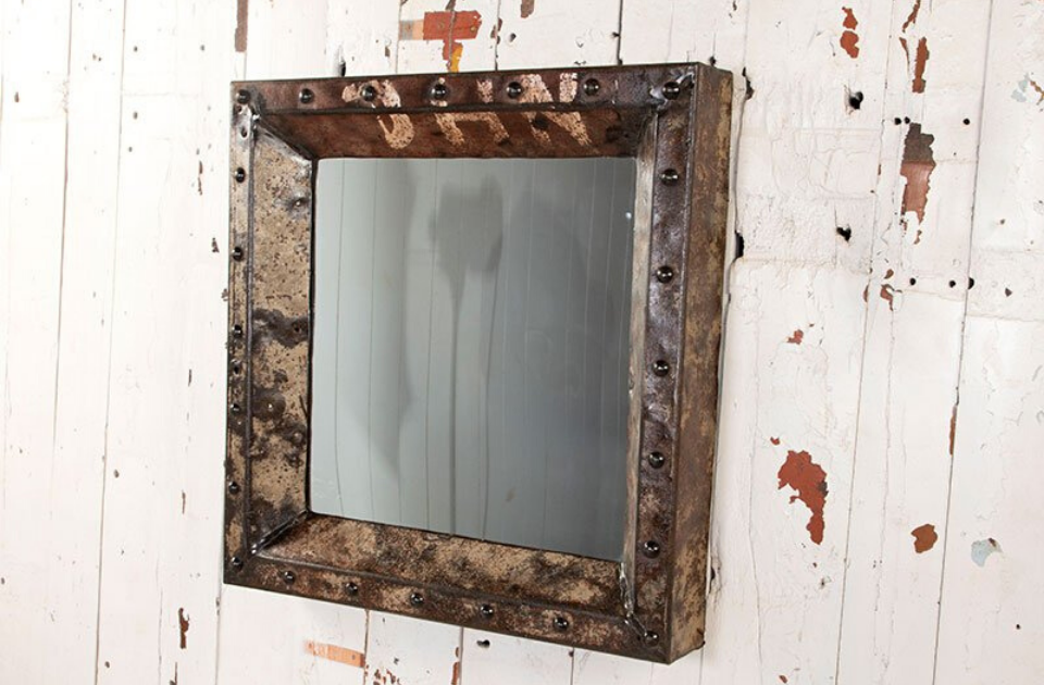 An iron-studded mirror hanging on a distressed white painted wall. 