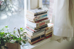 A pile of books and plants on a windowsill.