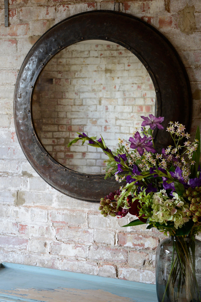 Large mirror hung on exposed brick wall next to flowers in vase